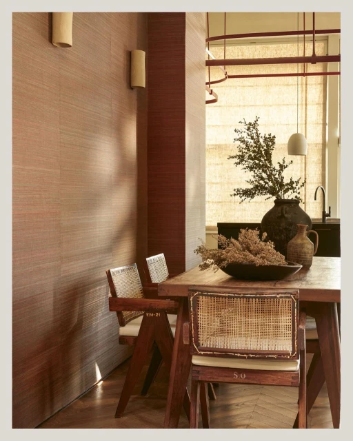 Interior view of a dining space with a wooden table, chairs, textural wall, and modern light fixture casting shadows.