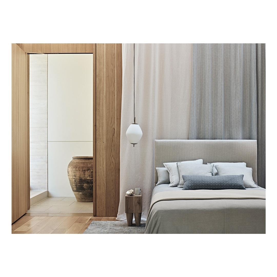 Modern bedroom with neutral tones featuring a bed with pillows and blankets, a wooden side table, and a glass pendant light.