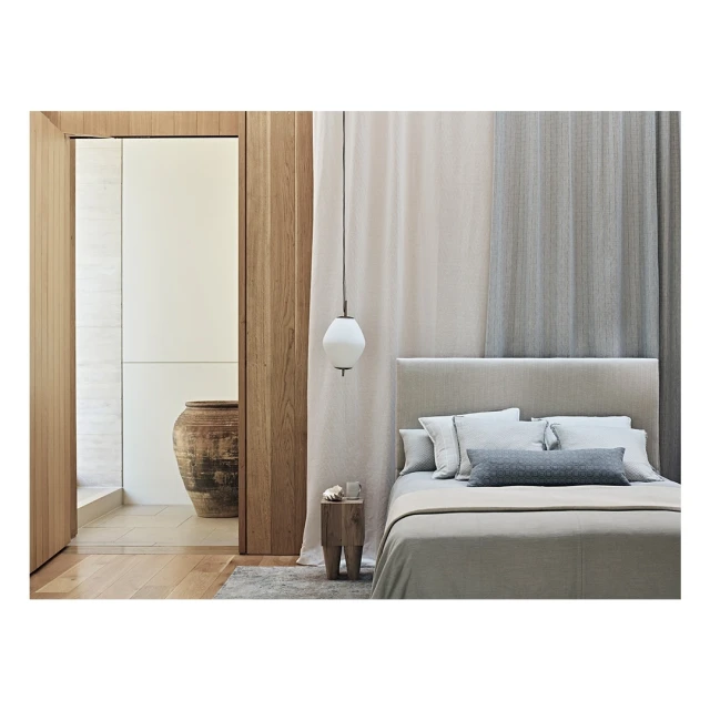 Modern bedroom with neutral tones featuring a bed with pillows and blankets, a wooden side table, and a glass pendant light.