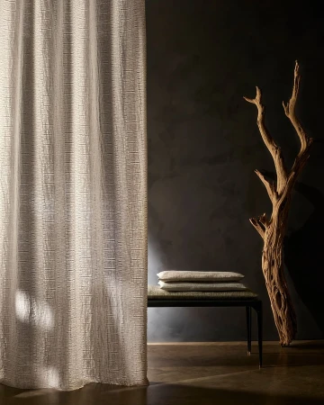Textured curtain panel in a neutral tone with natural driftwood sculpture, and a small bench with cushions against a dark wall.