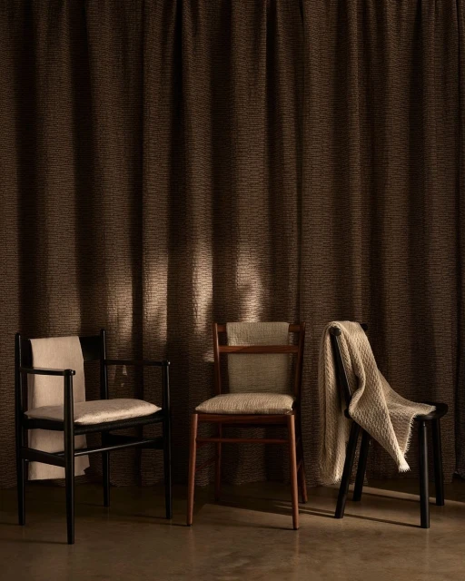 Interior design shot featuring three empty wooden chairs arranged in front of textured brown curtains, creating a minimalist aesthetic.