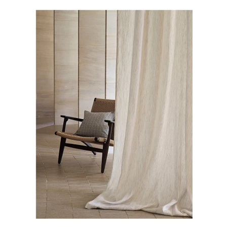Interior view of a woven chair with a striped cushion next to a light-colored curtain in front of a vertically paneled wall.