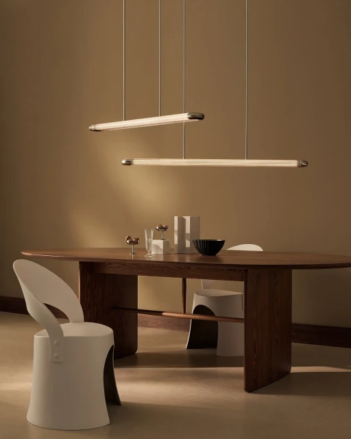 Minimalist interior featuring a wooden dining table with a black bowl and clear glasses, complemented by modern pendant lighting.