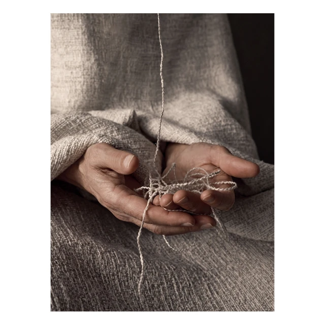 Close-up studio shot of an adult holding unraveling thread in their hands, showcasing texture and detail against a neutral backdrop.