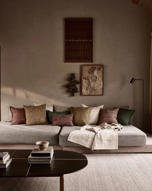 Neutral toned living room features a sectional sofa adorned with an array of decorative pillows, complemented by artwork and a dark coffee table.