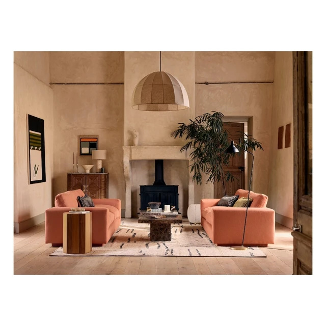 Living room interior featuring two coral-colored sofas, a patterned rug, fireplace, and contemporary lighting in a neutral palette.