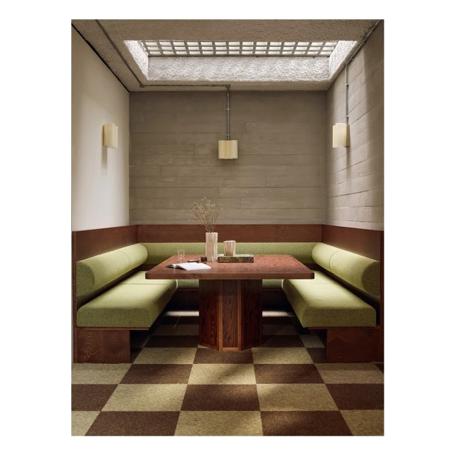 Interior view of a cozy booth with green cushions and a dark wood table under a skylight, complemented by a checkered floor pattern.