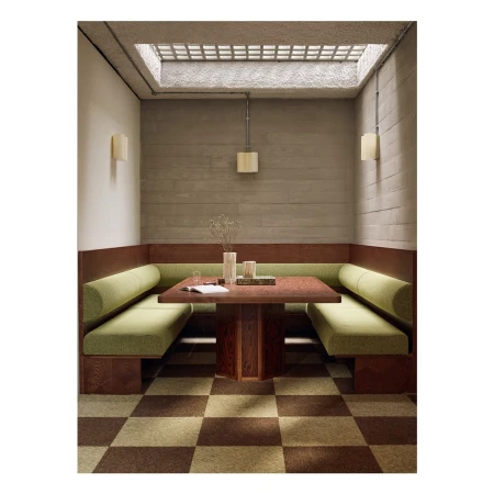 Interior view of a cozy booth with green cushions and a dark wood table under a skylight, complemented by a checkered floor pattern.