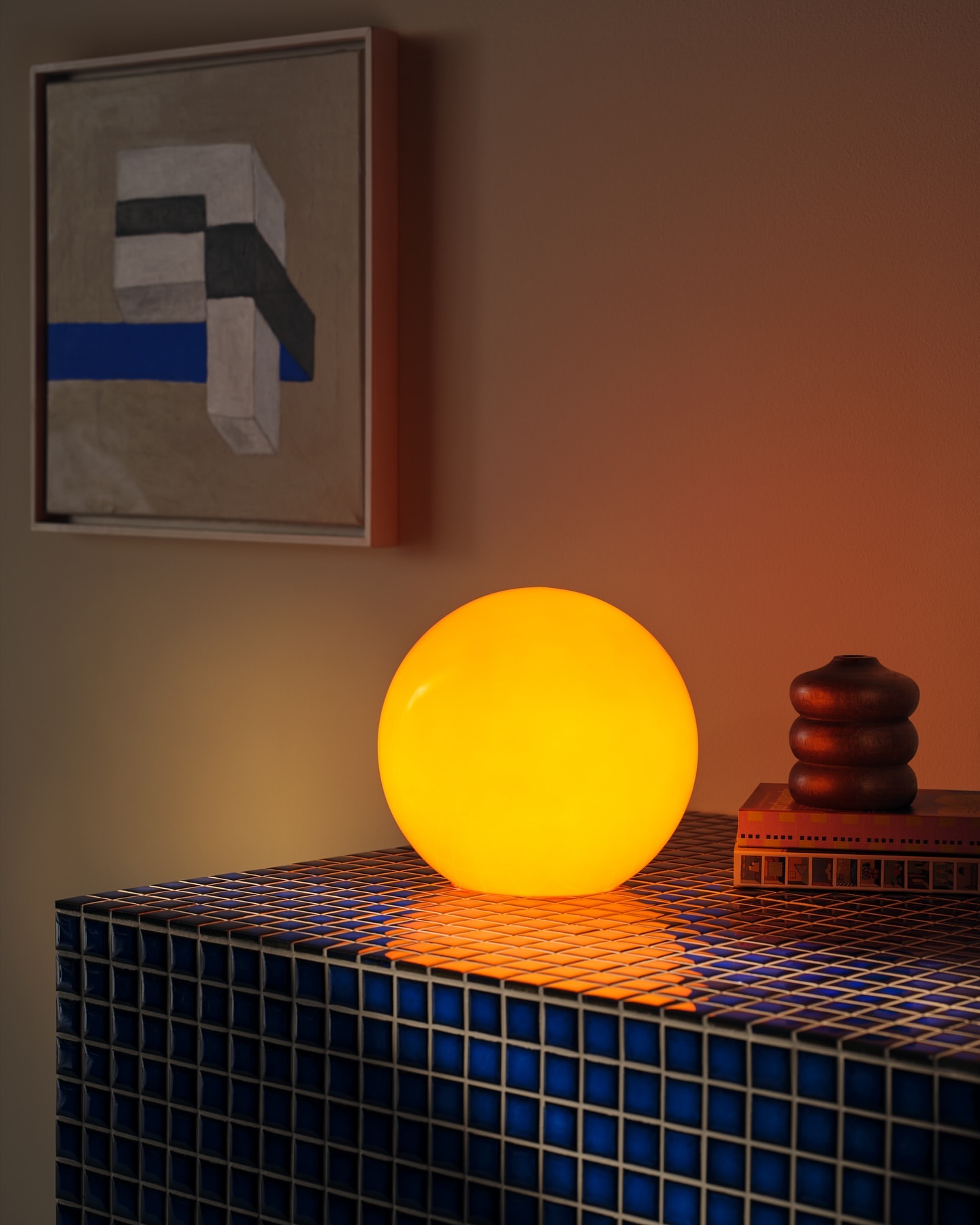 Illuminated spherical lamp on a blue tiled surface with a painting on the wall creates a warm, inviting indoor scene.