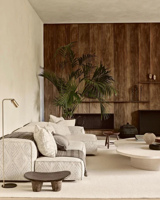 Living room interior featuring a patterned sofa, light rug, dark wood accent wall, potted plant, and neutral tones in a modern setting.