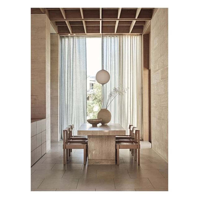Modern dining room interior with a light wood table and chairs, a large vase with flowers, and a globe light fixture.