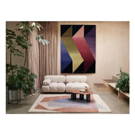 Living room interior featuring a modular cream sofa, geometric rugs and wall hanging, neutral walls, and potted plants for a modern aesthetic.
