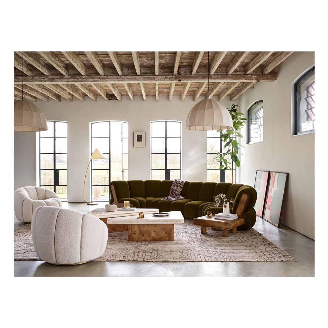 Living room interior with a large green sectional sofa, beige chairs, and modern coffee tables under a wooden beam ceiling.