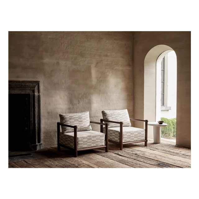 Interior design featuring two armchairs with patterned cushions in a room with rustic walls and a dark fireplace, creating a cozy setting.