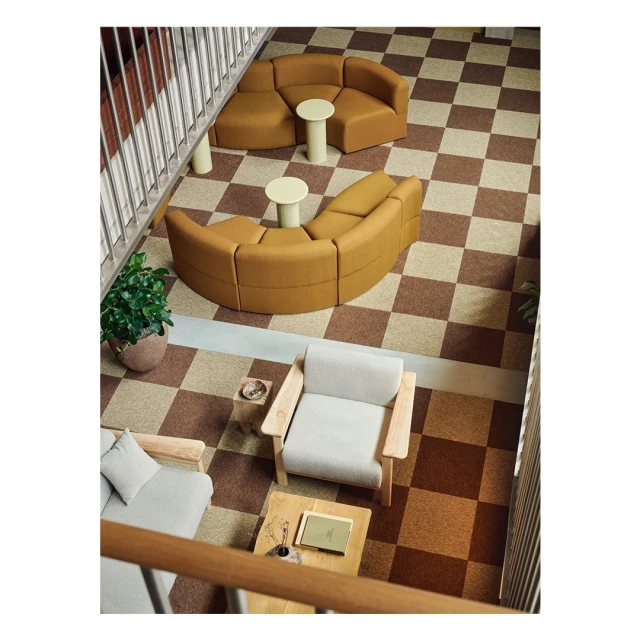 Interior view featuring modular mustard-colored sofas, light wood accent tables, checkered brown and beige flooring, and potted plant.