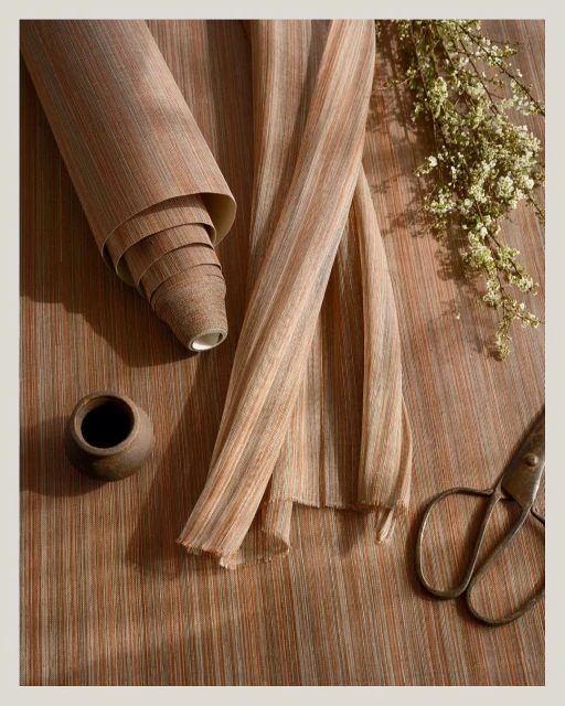 Roll of textured wallpaper alongside cut lengths, styled with ceramic vase, antique scissors, and sprigs of white flowers on wood-grain surface.