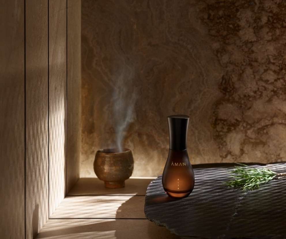 Aman essential oil in a dark brown glass bottle with a diffuser on a stone surface in a warm spa setting, wellness concept.