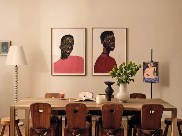 Interior dining room featuring a wooden table with chairs, artwork on the wall, flowers in a vase, and a standing lamp.