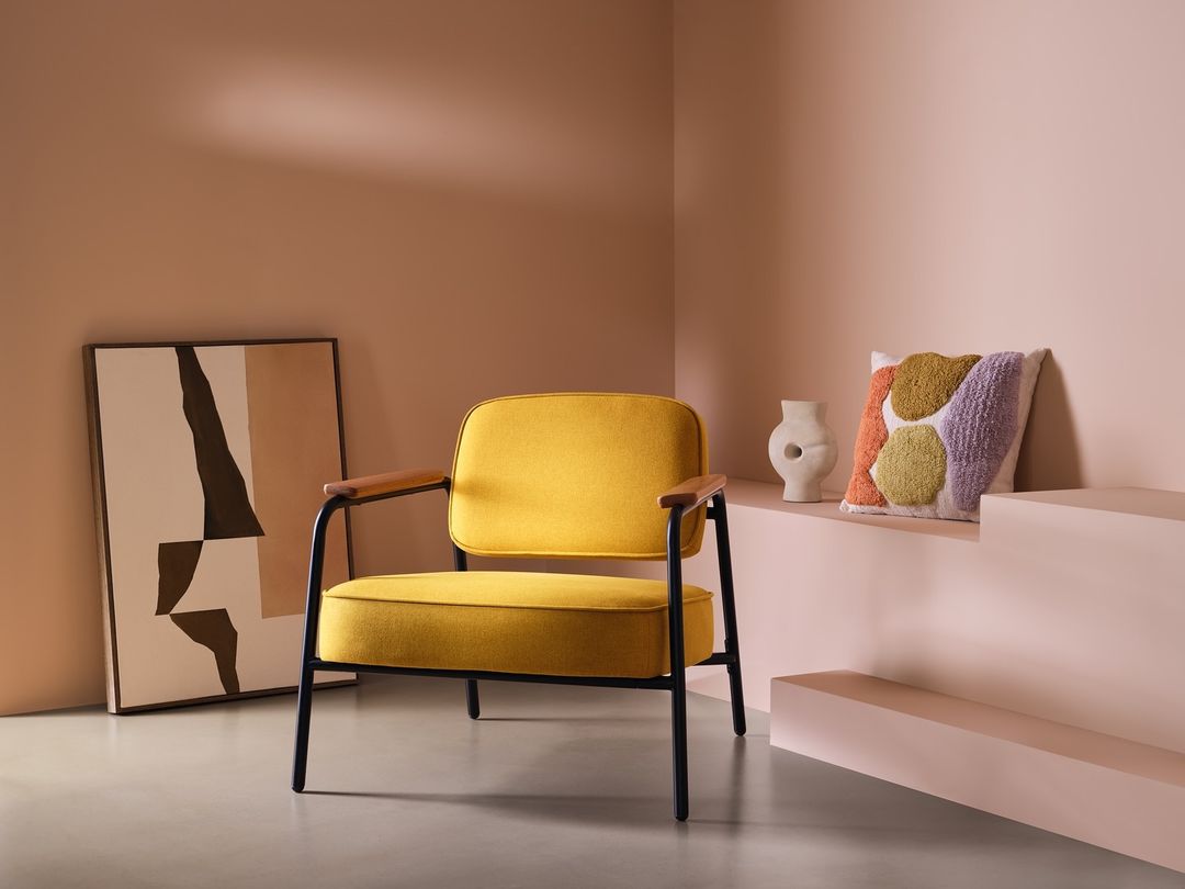 Contemporary living room interior with yellow upholstered armchair, abstract artwork, and geometric pillow against a peach-toned wall.