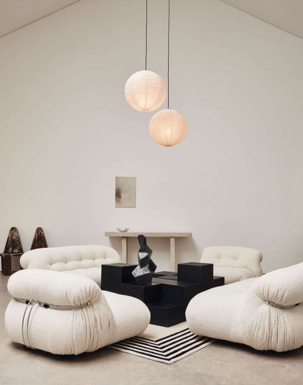 Interior with unique white lounge chairs, black geometric coffee table, white walls, and hanging round paper lanterns.