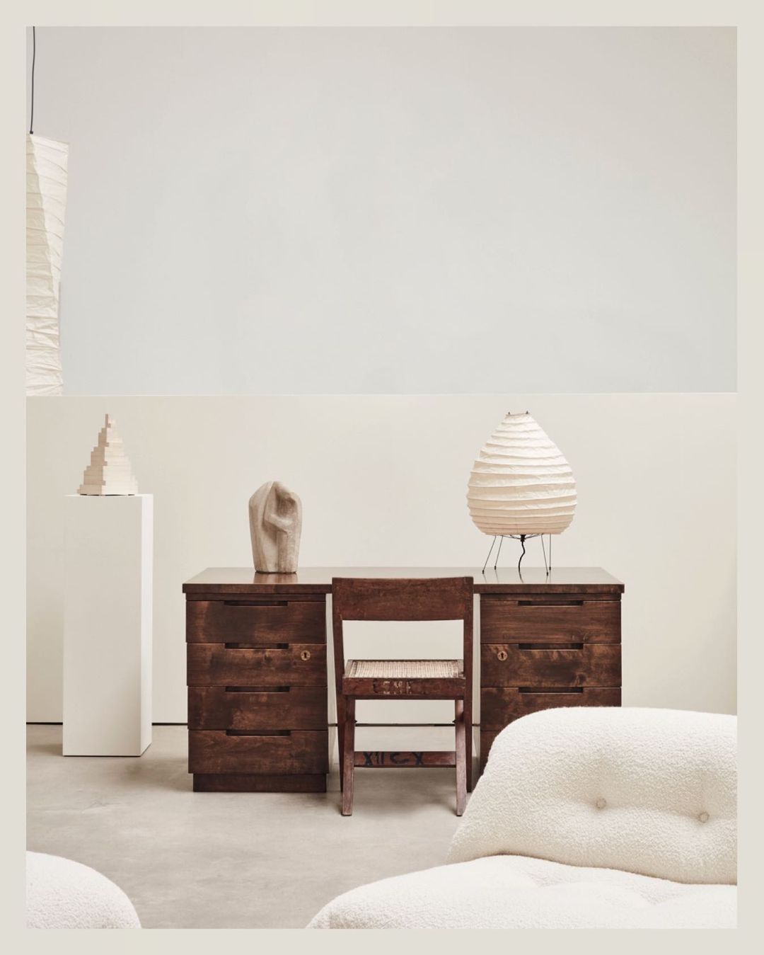 Interior shot of a dark wood desk and chair with white lamp and decorative objects on a neutral background, minimalist composition.
