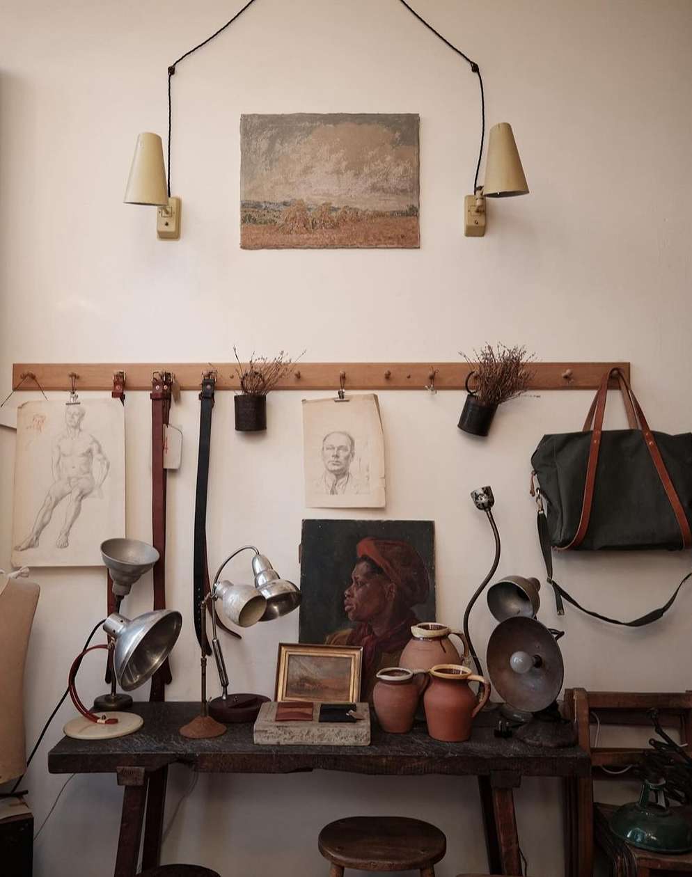 Interior still life featuring a wooden table with vintage lamps, pottery, and framed art, complemented by wall-mounted sconces and decor.
