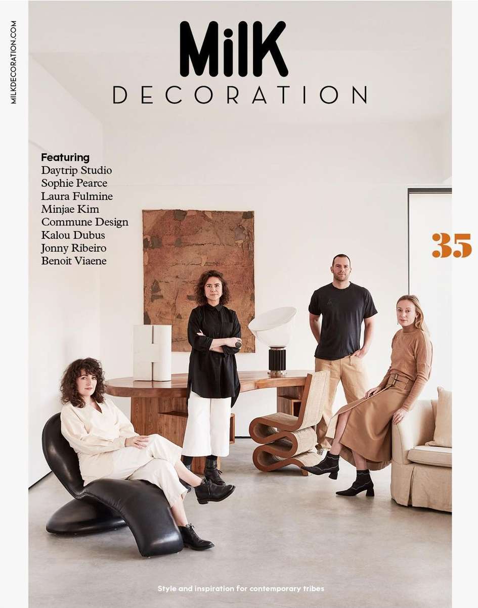 Milk Decoration magazine cover featuring four people in a modern interior. The magazine is centered with a wooden table and unique chairs.