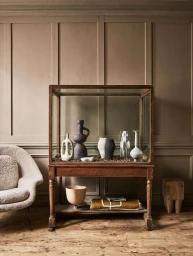 A wooden glass display case holding ceramic vessels, set against wood panel walls photographed by Jake Curtis