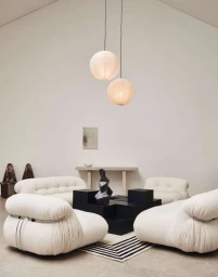 White textured modular armchairs arranged around a black coffee table under two spherical paper pendant lights.