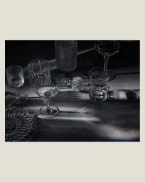 Still life photography of various crystal glassware and decanters casting dramatic light patterns on a dark surface.