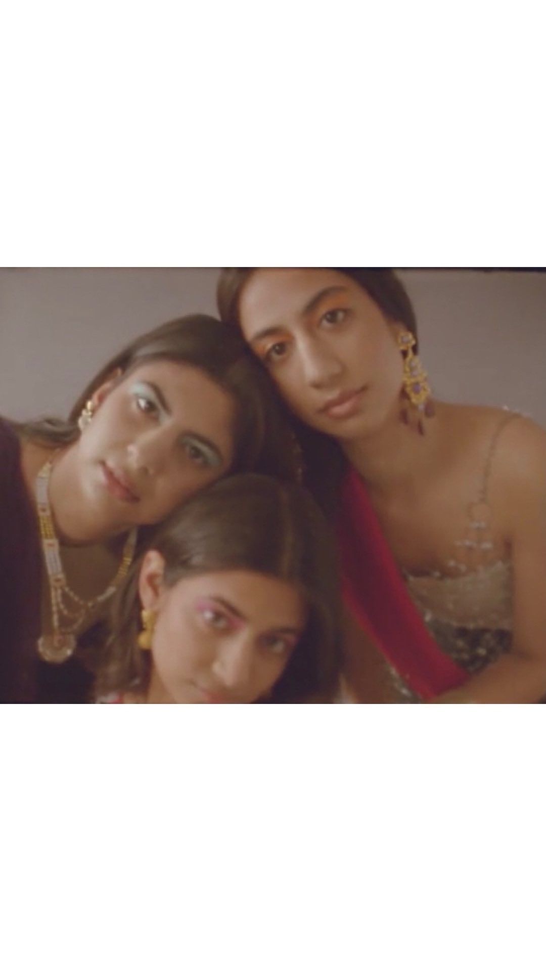 Three women pose together indoors with eye makeup and jewellery. One woman is wearing a red shawl and a beaded top.
