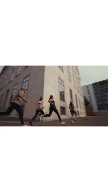 Four adults run along a city street next to a tall building on a cloudy day. They are wearing athletic clothes and running shoes.
