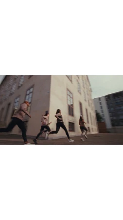 Four adults run along a city street next to a tall building on a cloudy day. They are wearing athletic clothes and running shoes.