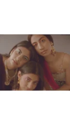 Three young women posed closely together wearing traditional jewellery and detailed garments in a softly lit portrait by Jameela Elfaki.