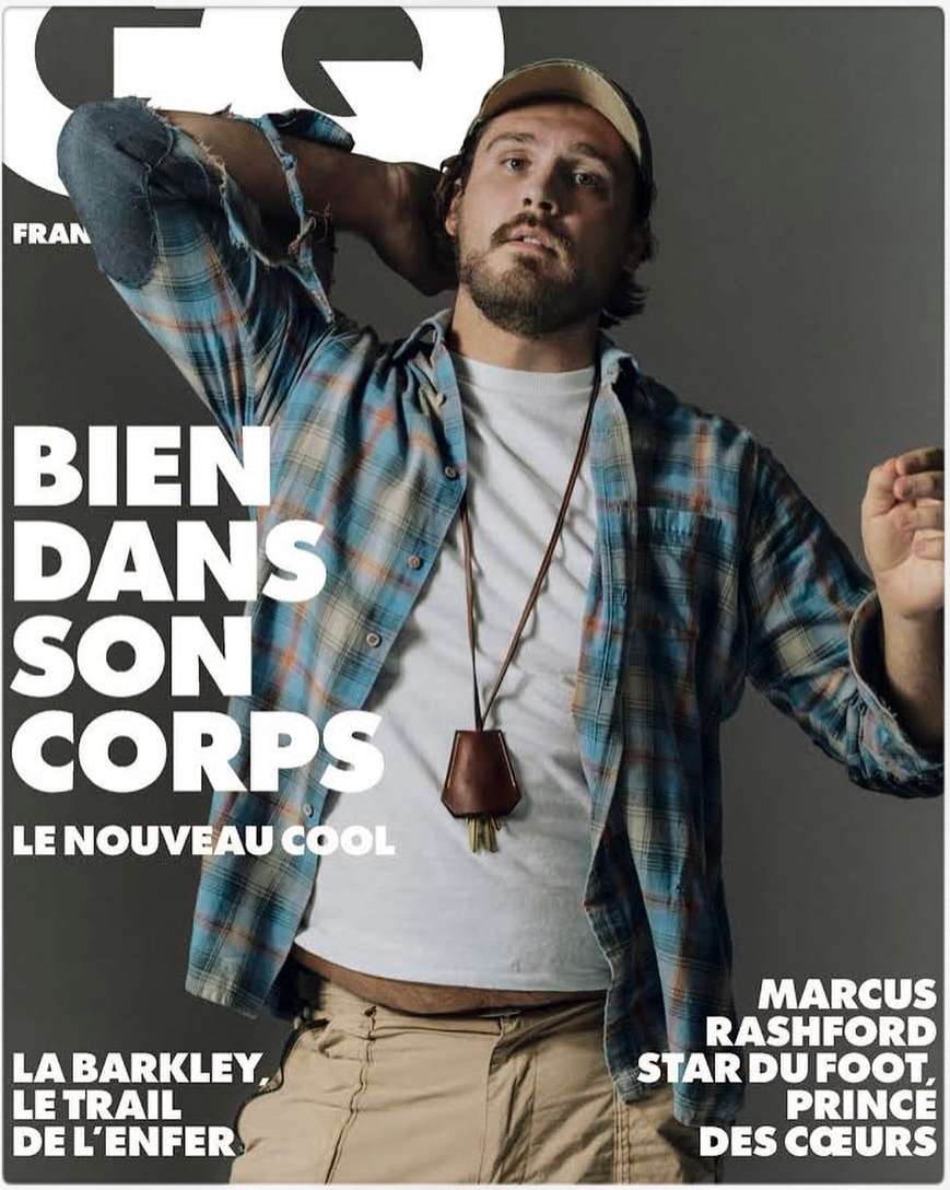 GQ magazine cover featuring a man wearing a plaid shirt, hat, and necklace, posing against a neutral gray background with magazine text.