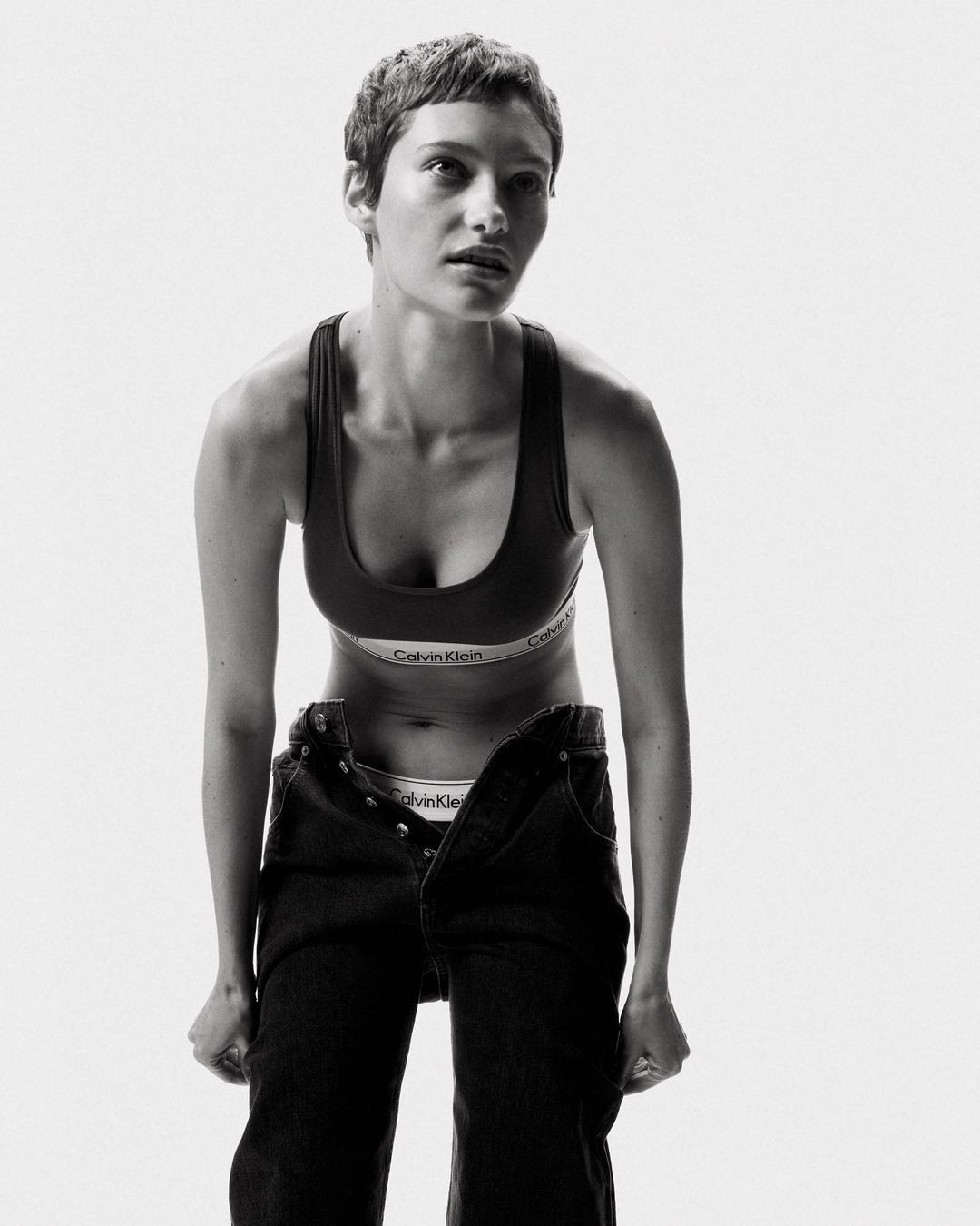 Monochrome portrait of a woman in athletic wear and jeans in a white studio setting, emphasizing natural beauty and fashion.