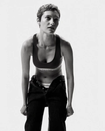 Monochrome portrait of a woman in athletic wear and jeans in a white studio setting, emphasizing natural beauty and fashion.