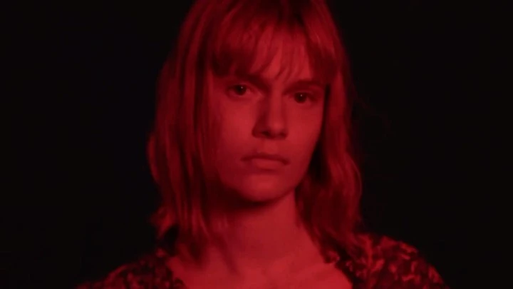Close-up of an adult female with red hair and dark floral top, gazing directly at the camera against a dark background, monochrome red.