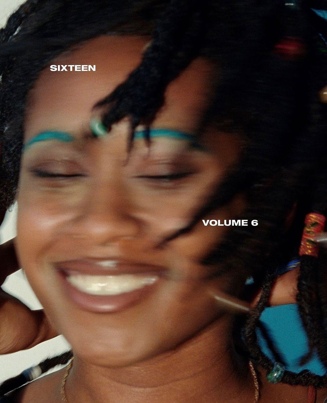 Close-up portrait of a smiling black woman with dark braided hair and teal eyebrows; image has a blurred, dreamy aesthetic.