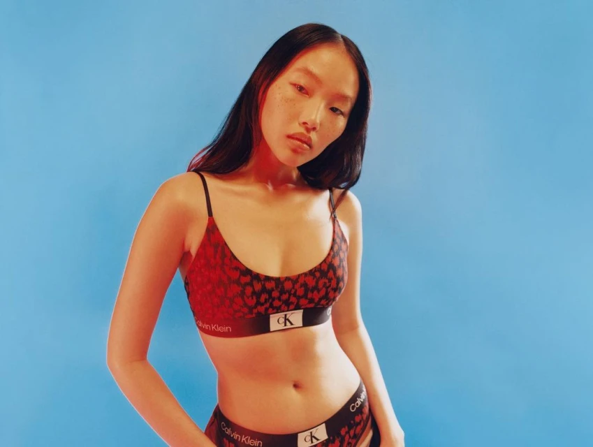 An Asian female model poses in Calvin Klein lingerie against a bright blue backdrop, showcasing the brand's lingerie collection.