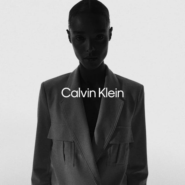 Black and white portrait of a Black adult female wearing a blazer. Calvin Klein logo is visible on the blazer in a studio setting.