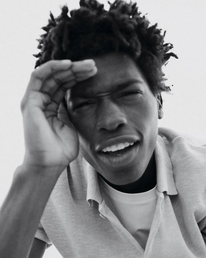 Black and white portrait of a young man holding his hand to his forehead, shielding his eyes.