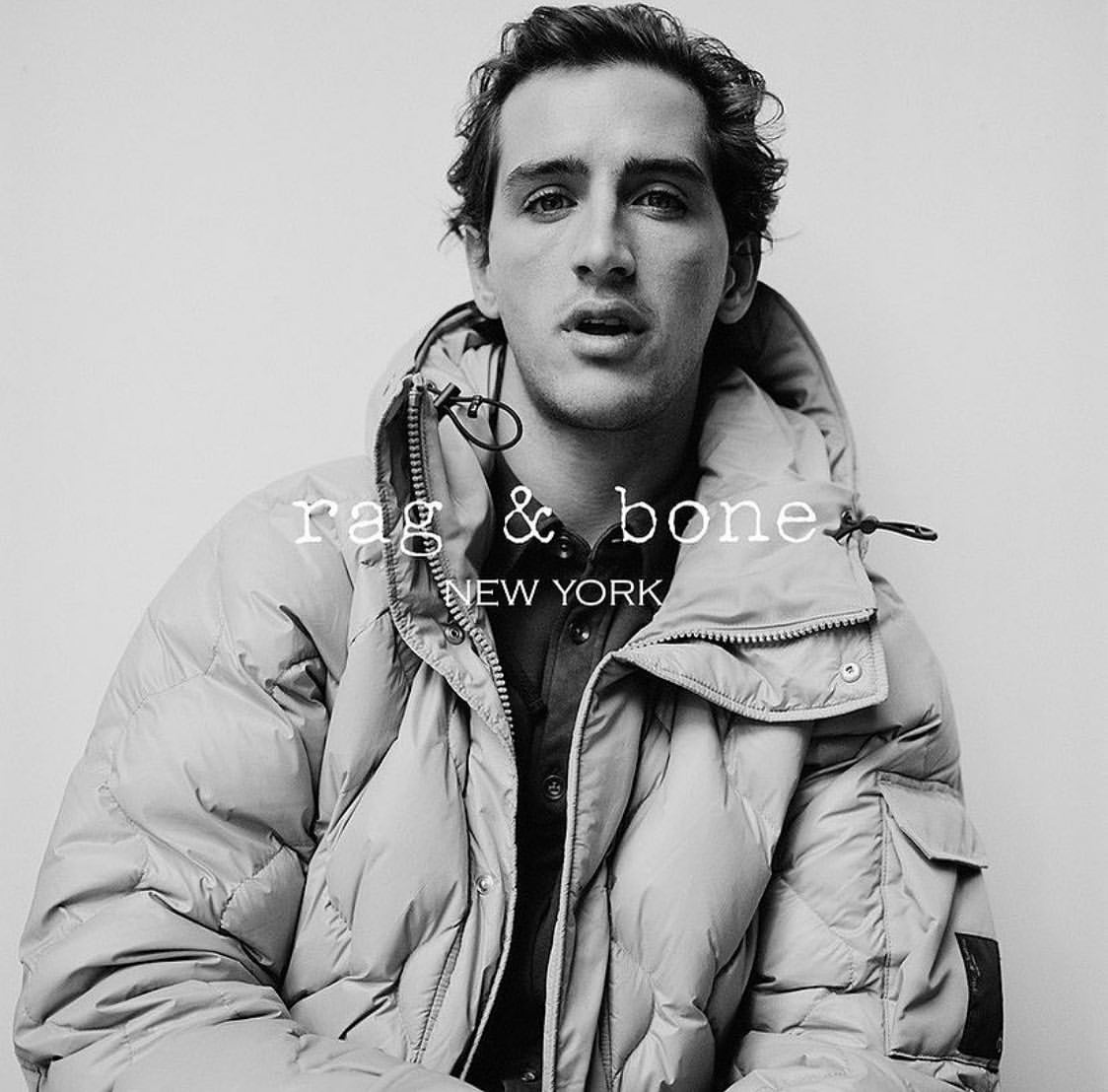 Monochrome portrait of a man wearing a quilted puffer jacket against a plain background.