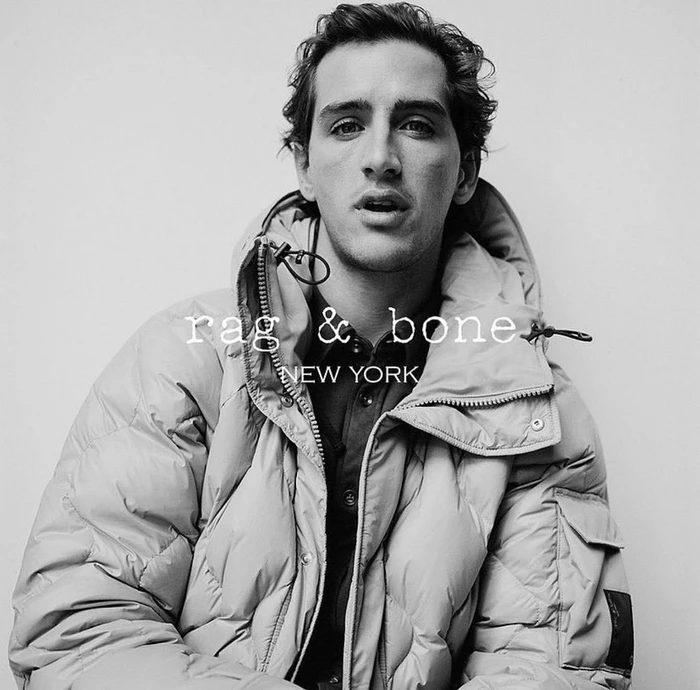 Monochrome portrait of a man wearing a quilted puffer jacket against a plain background.