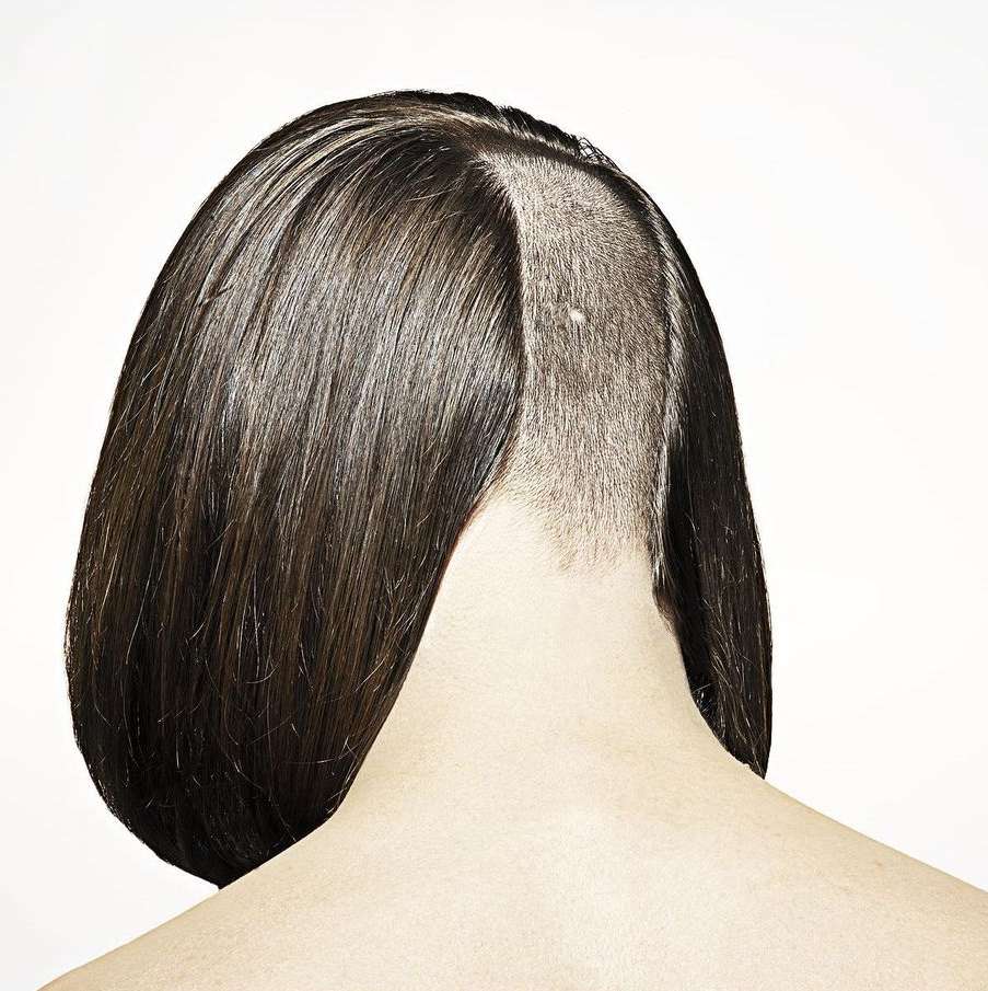 Close-up shot of the back of a woman's head with short brown hair, featuring an undercut style on a white studio background.