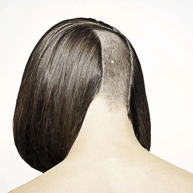 Close-up shot of the back of a woman's head with short brown hair, featuring an undercut style on a white studio background.