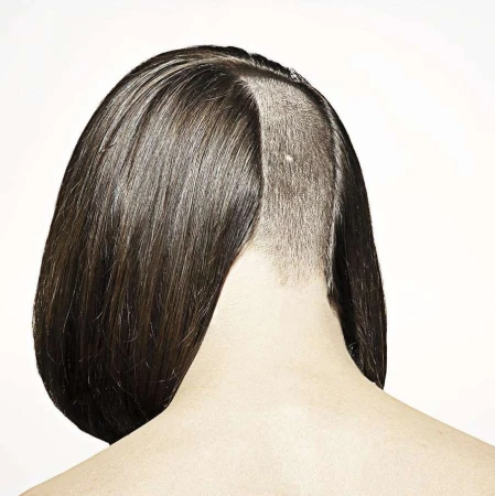 Close-up shot of the back of a woman's head with short brown hair, featuring an undercut style on a white studio background.