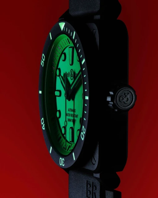 Close-up of a black Bell & Ross watch with a green luminescent face against a red background, showcasing its unique square design and readability.