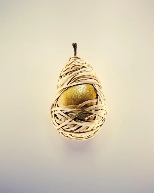 Golden pear wrapped with tan paper strips on a light yellow background in a studio setting. Food and product photography.