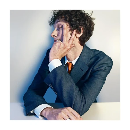 Adult male in business suit poses in a photo studio with his fingers on his face, wearing an orange tie. Head and shoulder shot.
